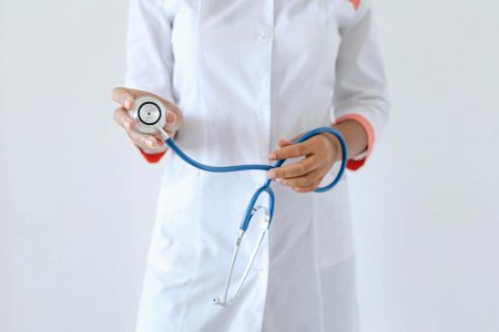 Osoba w białym kitlu trzyma w rękach niebieski stetoskop