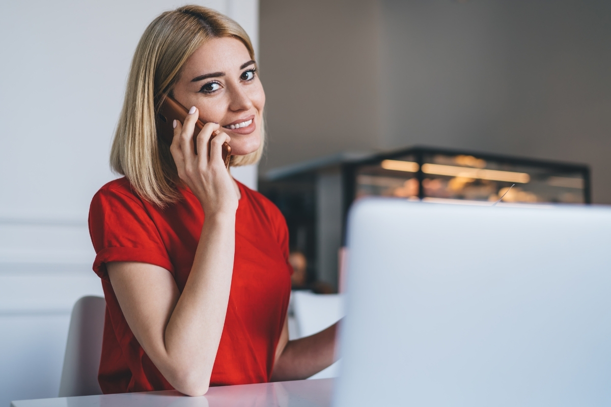 Uśmiechnięta pani z działu Biura Obsługi Klienta 
        w czerwonej koszulce rozmawia przez telefon przy laptopie
